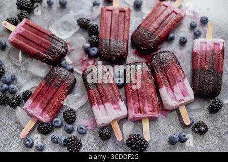 Hausgemachte brombeer- und Sahneeis oder Eis mit gefrorenen Beeren auf einem Tablett aus schwarzem Schiefer vor dunklem Hintergrund. Draufsicht, flach Stockfoto