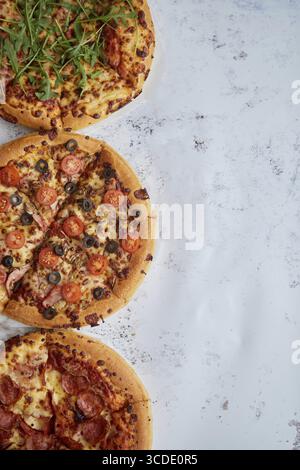 Drei verschiedene Arten von Pizzen. In einer Reihe auf weißem rostigem Tisch platziert. Ansicht von oben mit einem Leerzeichen für Ihren Text Stockfoto
