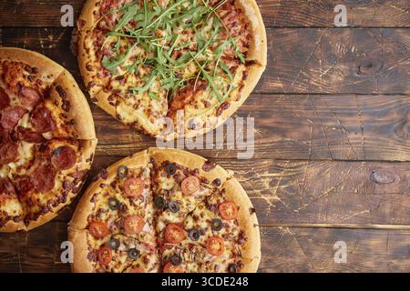 Komposition von drei verschiedenen Pizzen auf einem rostigen, zerkratzten Holztisch. Warme und frische Speisen, die verzehrfertig sind Stockfoto