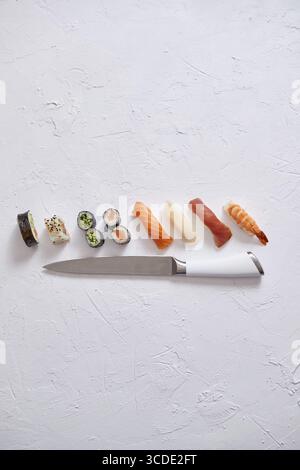 Verschiedene Sushi-Rollen mit japanischem Messer auf weißem Steinschieferhintergrund. Mit Kopierraum für Text. Draufsicht Stockfoto