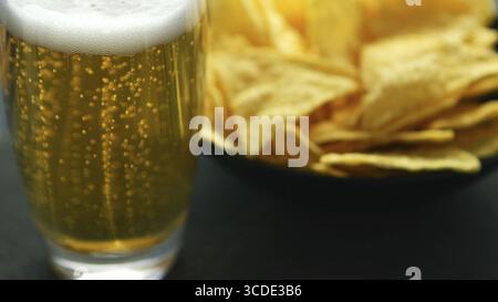 Transparente Glas helles Bier mit Schaum und Schüssel mit knusprigen golden Nacho Chips am Tisch serviert. Stockfoto