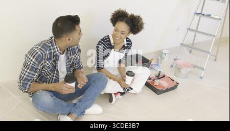 Junges Paar, eine Pause von redecorating ihr neues Zuhause sitzen auf dem Boden mit Tassen Kaffee zum mitnehmen im Chat Stockfoto