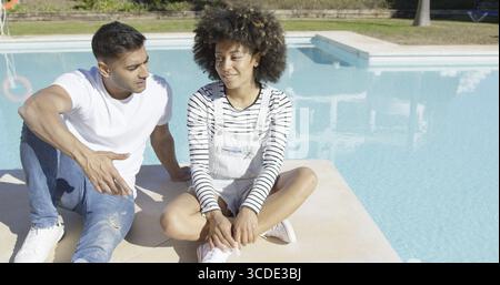 Junges Paar zum Entspannen in der Sonne an einem Pool auf der gefliesten Surround im Chat sitzen und Lächeln Stockfoto