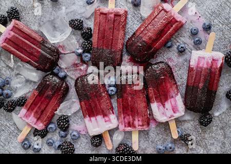 Hausgemachte brombeer- und Sahneeis oder Eis mit gefrorenen Beeren auf einem Tablett aus schwarzem Schiefer vor dunklem Hintergrund. Draufsicht, flach Stockfoto