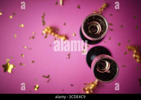 Zwei Gläser Sekt mit goldenem Dekor aus Konfetti und Serpentinen auf rosa Hintergrund. Draufsicht mit Kopierbereich. Festlich Stockfoto