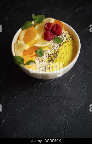 Leckerer Orangensaft oder Joghurt, serviert in einer Schüssel. Mit frischen Himbeeren, Orangenscheiben, Chiasamen, Hafer. Auf Steintisch. Mit Kopierraum Stockfoto