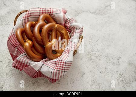 Brotkorb mit rot-weiß karierter Serviette gefüllt mit frischen braunen Brezeln. Draufsicht. Auf Steintisch Stockfoto