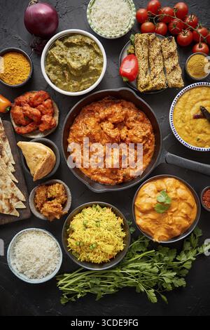 Verschiedene indische Gerichte auf einem Tisch. Scharfes Huhn Tikka Masala in einer Eisenpfanne. Serviert mit Reis, Naan und Gewürzen. Verschiedene indische Gerichte Stockfoto