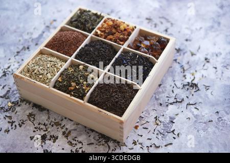 Verschiedene Arten von trockenem Tee - grün, schwarz, rot, Obst und blau in Holzkiste auf dem Tisch. Draufsicht. Tee-Zeit-Konzept Stockfoto