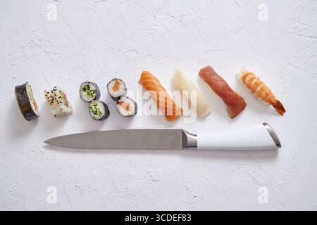 Verschiedene Sushi-Rollen mit japanischem Messer auf weißem Steinschieferhintergrund. Mit Kopierraum für Text. Draufsicht Stockfoto