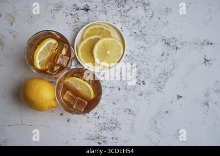 Whiskey-Sauergetränk mit Zitrone im Glas auf rustikalem Steinhintergrund. Zwei Gläser mit Eis und Karaffe Stockfoto