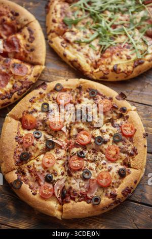 Komposition von drei verschiedenen Pizzen auf einem rostigen, zerkratzten Holztisch. Warme und frische Speisen, die verzehrfertig sind Stockfoto