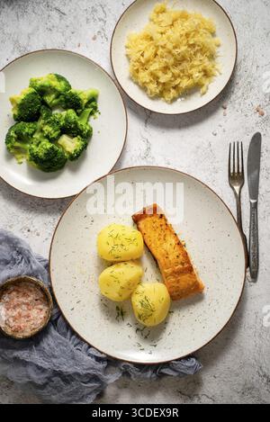 Hausgemachter gebackener Lachs serviert mit Populaten, Brokkoli und Sauerkraut. Leckeres und köstliches Essen. Draufsicht, flach liegend Stockfoto