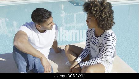Young African American Paar mit einem schweren Chat sitzen zusammen in der heißen Sommersonne auf der gepflasterten Umrahmung eines Schwimmbades Stockfoto