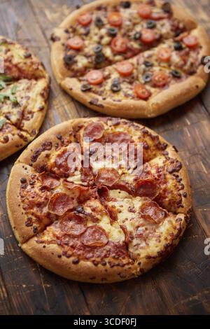 Komposition von drei verschiedenen Pizzen auf einem rostigen, zerkratzten Holztisch. Warme und frische Speisen, die verzehrfertig sind Stockfoto