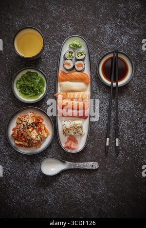 Asiatische Küche. Verschiedene Sushi-Rollen auf Keramikplatten. Kimchi und goma Wakame Salate. Sojasuppe und Essstäbchen an den Seiten. Grungy Dark bac Stockfoto