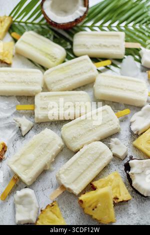Sommereiskel am Stock. Pinacolada-Geschmack. Hergestellt aus Ananas, Kokontomilch und Rum. Veganer Snack. Mit frischem Obst dekoriert. Draufsicht. Flache Lagen Stockfoto