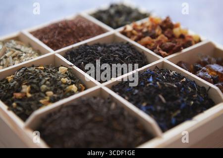 Verschiedene Arten von trockenem Tee - grün, schwarz, rot, Obst und blau in Holzkiste auf dem Tisch. Draufsicht. Tee-Zeit-Konzept Stockfoto
