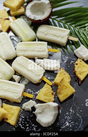 Sommereiskel am Stock. Pinacolada-Geschmack. Hergestellt aus Ananas, Kokontomilch und Rum. Veganer Snack. Mit frischem Obst dekoriert. Draufsicht. Flache Lagen Stockfoto