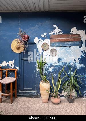 Rustikale blaue Wand mit Pflanzen, Holzstuhl, Strohhut und persischen Tellern im Charkh Café in Rasht, Iran. Stockfoto