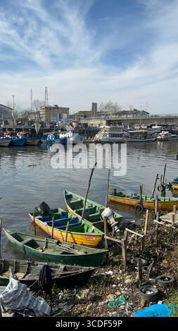 Farbenfrohe Fischerboote an der Uferpromenade von Bandar Anzali im Norden des Iran, mit größeren Schiffen und Hafengebäuden im Hintergrund. Stockfoto