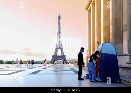 Ein Paar bereitet sich auf ein Fotoshooting bei Sonnenaufgang am Eiffelturm in Paris vor, mit einem ausklappbaren Zelt und anderen Fotografen im Hintergrund. Stockfoto