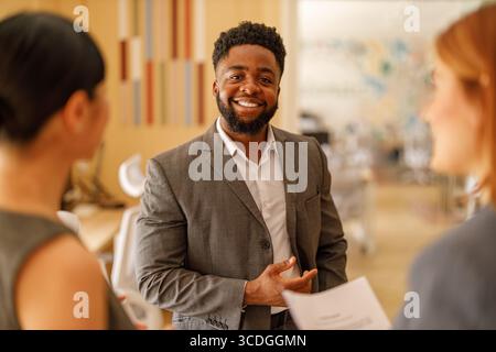 Porträt eines selbstbewussten männlichen Managers, der in die Kamera lächelt, während er mit weiblichen Profis bei Geschäftstreffen steht Stockfoto