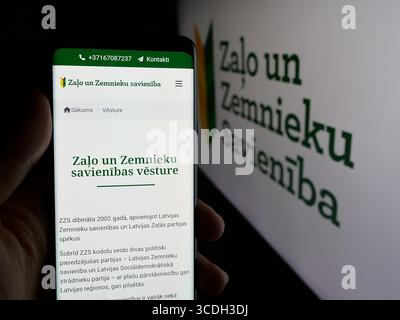 Stuttgart, Deutschland - 28. 07. 2025: Person, die ein Handy hält, mit Webseite der Partei Zalo un Zemnieku Savieniba (ZZS) vor dem Logo auf dem Bildschirm. Stockfoto