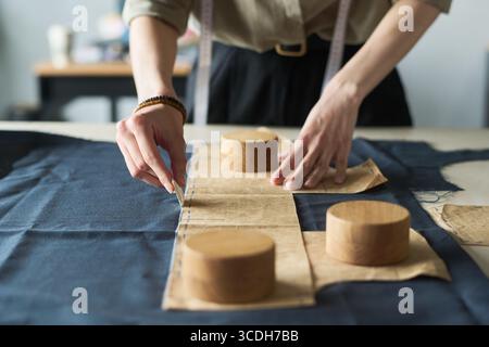 Junge Erwachsene kaukasische Frau, die den Stoff mit Schneiderkreide markiert, während sie Papiernähmuster und Mustergewichte auf dem Arbeitstisch hält, wobei der Schwerpunkt auf präzisem Bekleidungsprozess liegt Stockfoto