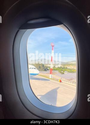 Vertikale Aufnahme eines Flugzeugfensters mit Blick auf die Landebahn. Vertikales Bild, ideal für Reise- und Tourismusbüros. Stockfoto