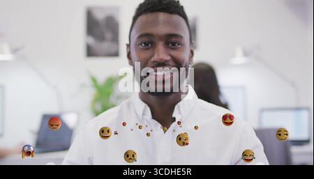 Lächelnder Büroangestellter mit weißem Hemd im modernen Großraumbüro, mit schwimmenden Emojis Stockfoto