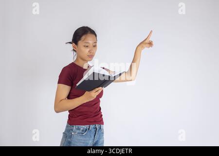 Die Frau hält ein Buch und zeigt nach oben, möglicherweise zeigt oder erklärt sie etwas, was sie liest. Stockfoto