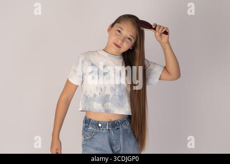 Das Mädchen hält ihr sehr langes, glattes Haar mit einer Hand, während es zur Kamera blickt Stockfoto