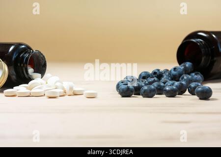 Weiße Pillen und Heidelbeeren aus braunen Flaschen auf Holzoberfläche verschüttet Stockfoto