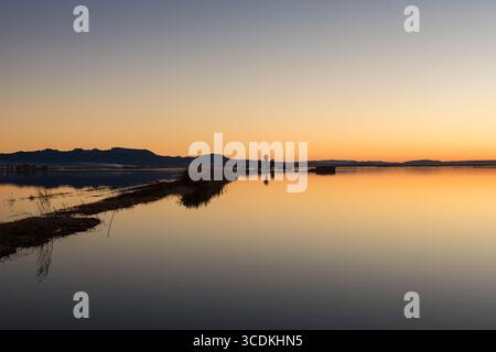 Die Abenddämmerung lässt sich über Valencias Albufera-Reisfeldern nieder und malte die Szene mit Orangentönen und ruhigen Wasserreflexionen, die von einem rustikalen Holzklopfer akzentuiert werden Stockfoto
