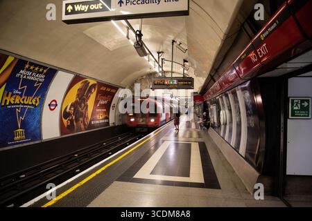 Zentrale Bahnsteig an der Holborn U-Bahn Station, London, mit einer roten U-Bahn, die sich unter berühmten Rundschildern und Bahnhofsbeleuchtung nähert. Stockfoto