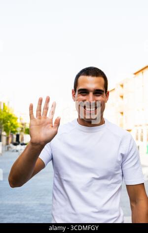 Junger Mann lächelt und winkt in urbaner Umgebung Stockfoto