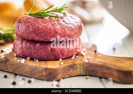 Rohe Burger Beef Patties auf Schneidebrett auf einem weißen Tisch. Stockfoto