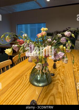 Das Bild zeigt eine mit Wasser gefüllte klare Glasvase mit einem Strauß von Lisianthus-Blüten in Pastellfarben wie Gelb, Lila, weiß und Stockfoto