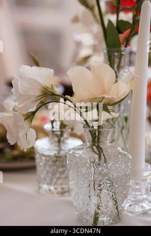 Ein Nahaufnahme-Stillleben fängt zarte weiße süße Erbsenblüten ein, die anmutig in verschiedenen Kristallvasen angeordnet sind, um eine raffinierte Hochzeit oder ein Ereignis zu kreieren Stockfoto