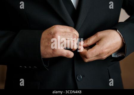 Eine Nahaufnahme zeigt einen Mann, der seine dunkelschwarze Anzugsjacke ordentlich zuknöpft und eine professionelle Ästhetik darstellt. Das Bild vermittelt Eleganz und Stockfoto