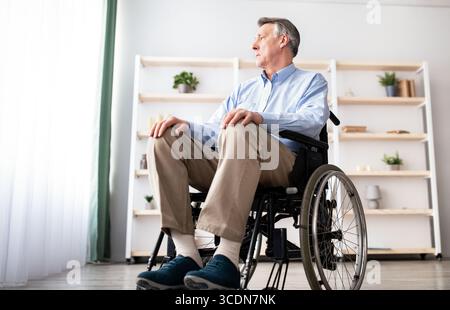 Low-Angle-Ansicht von beeinträchtigten männlichen Patienten im Rollstuhl Blick aus dem Fenster, fühlen traurig und verzweifelt zu Hause Stockfoto