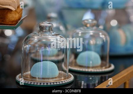 Diese Aufnahme zeigt zarte, pastellblaue Macarons, die unter klaren Glasuhren in einer charmanten Bäckerei präsentiert werden und eine Vintage-Ästhetik unterstreichen Stockfoto