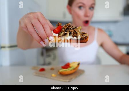 Frau in weißer Spitze bereitet Avocado Sandwich für gesundes Frühstück zu Hause Stockfoto