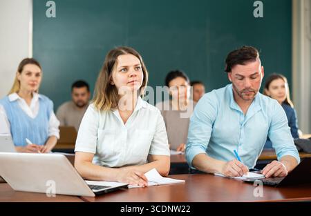 Gruppe von erwachsenen Schülern, die an Tischen im Klassenzimmer sitzen Stockfoto
