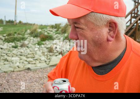 Reifer Kaukasier mit orangefarbener Baseballmütze und T-Shirt auf dem Schotterantrieb mit einer Aluminiumdose Dite-Coke, Edens Township, Gregory Cou Stockfoto