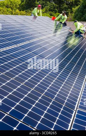 Männer mit Sicherheitsgurten, die auf dem Dach stehen und das LG NeonR installieren DC-Photovoltaikpaneele auf Aluminiumschienen bei einer Wohnphotovoltaik Installieren Stockfoto