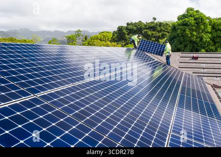 Männer mit Sicherheitsgurten, die auf dem Dach stehen und das LG NeonR installieren DC-Photovoltaikpaneele auf Aluminiumschienen bei einer Wohnphotovoltaik Installieren Stockfoto