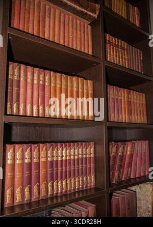 Tauranga Neuseeland - 26. Juni 2014; dunkles hölzernes Bücherregal mit Reihen gebundener Bücher gleicher Größe und Farbe in vertikaler Komposition. Stockfoto