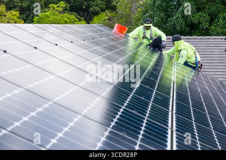 Männer mit Sicherheitsgurten, die auf dem Dach stehen und das LG NeonR installieren DC-Photovoltaikpaneele auf Aluminiumschienen bei einer Wohnphotovoltaik Installieren Stockfoto